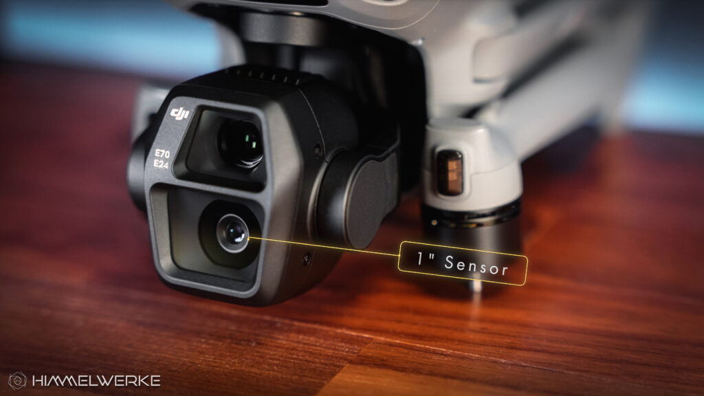 Das Kameramodul der DJI Air 3S in einer Nahaufnahme. Die Drohne liegt zusammengeklappt auf einem Holztisch. Ein Schriftzug mit "1" Sensor" weist mit gelber Umrandung und Linie auf den 1 Zoll sensor der Hauptkamera hin.