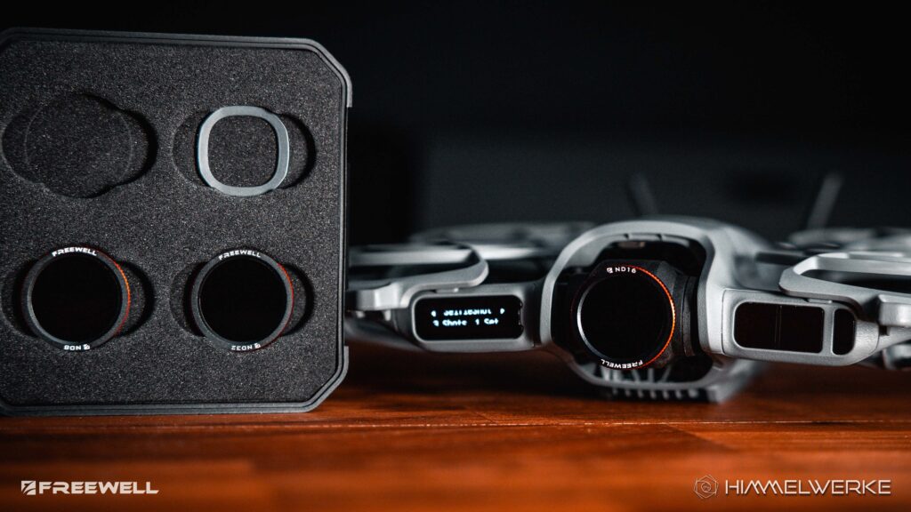 Ein Himmelwerke Bild zum DJI Neo 2 Test. DJI Neo 2 ND Filter von Freewell im Closeup. Einmal links das aufgestellte ND-Filtercase, wo man zwei Filter un einen magnetischen Ring erkennen kann und rechts daneben die Neo 2 auf einem Holztisch befindlich. Auf der Kamera ist bereits ein ND Filter von Freewell angebracht.